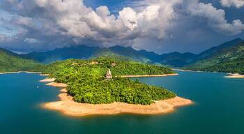 A lush green island with a temple in the center, surrounded by a calm blue lake and mountains in the background.