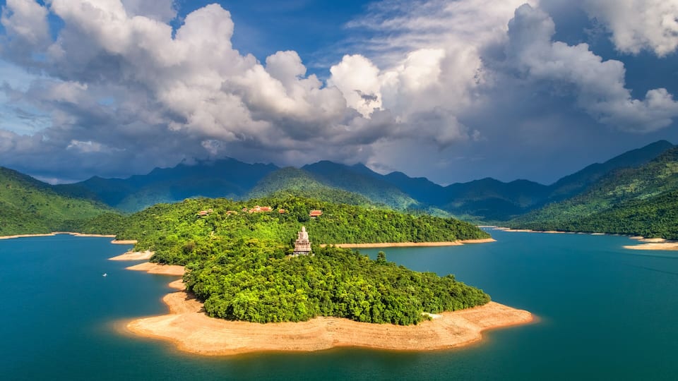 A lush green island with a temple in the center, surrounded by a calm blue lake and mountains in the background.
