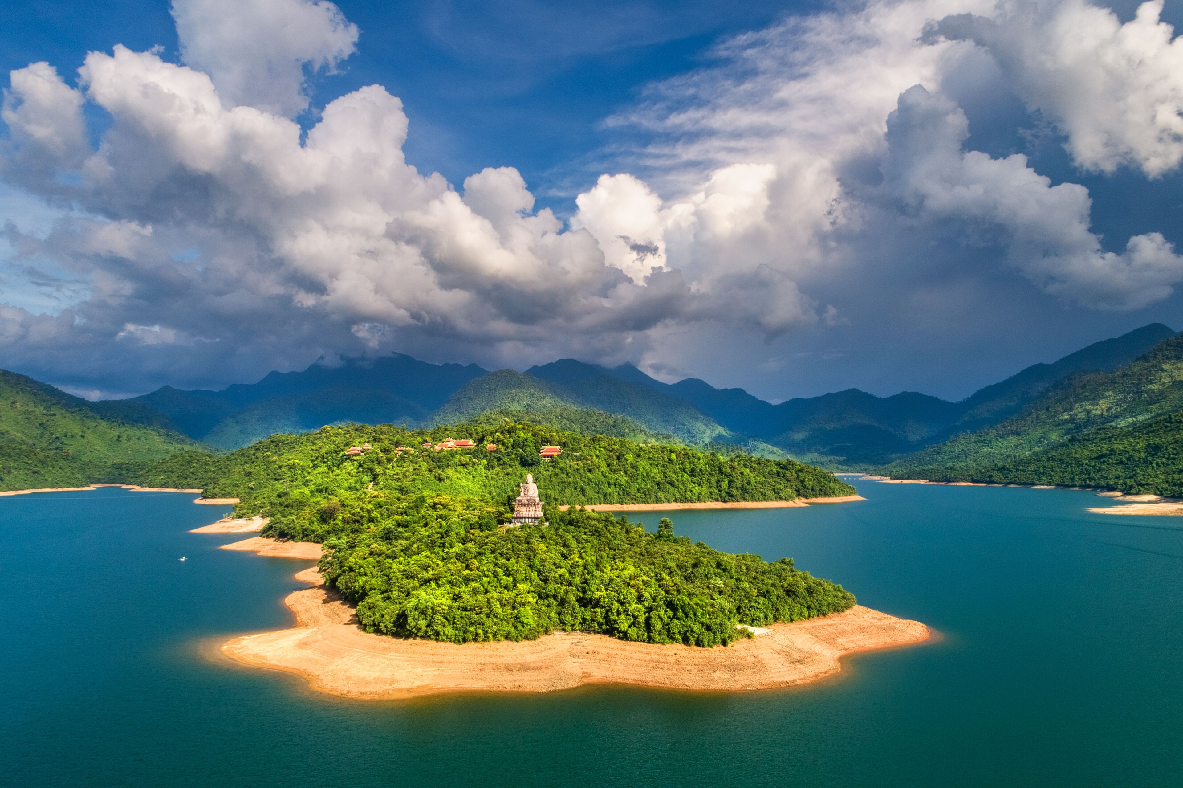 A lush green island with a temple in the center, surrounded by a calm blue lake and mountains in the background.