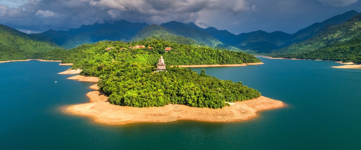 A lush green island with a temple in the center, surrounded by a calm blue lake and mountains in the background.