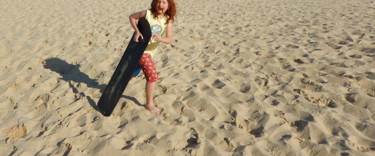 A child playing in a desert with sand dunes in the background.