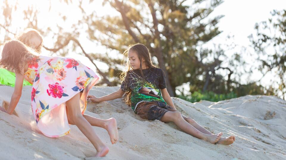 Three individuals on a sandy slope with trees in the background.