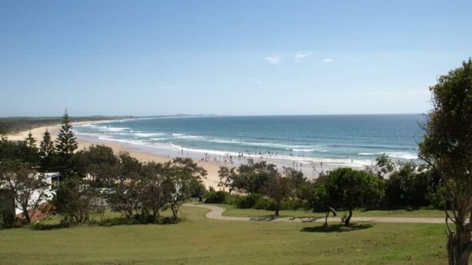 A coastal landscape with a beach, ocean, and grassy area with trees.