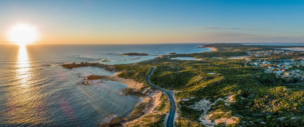 Scenic drive passing near ocean coastline and Beachport town at sunset - wide aerial panorama