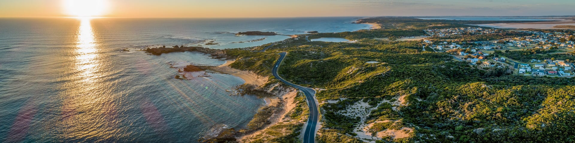 Scenic drive passing near ocean coastline and Beachport town at sunset - wide aerial panorama