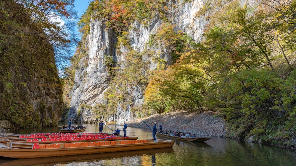 A river with boats, a rocky cliff, and autumn foliage.