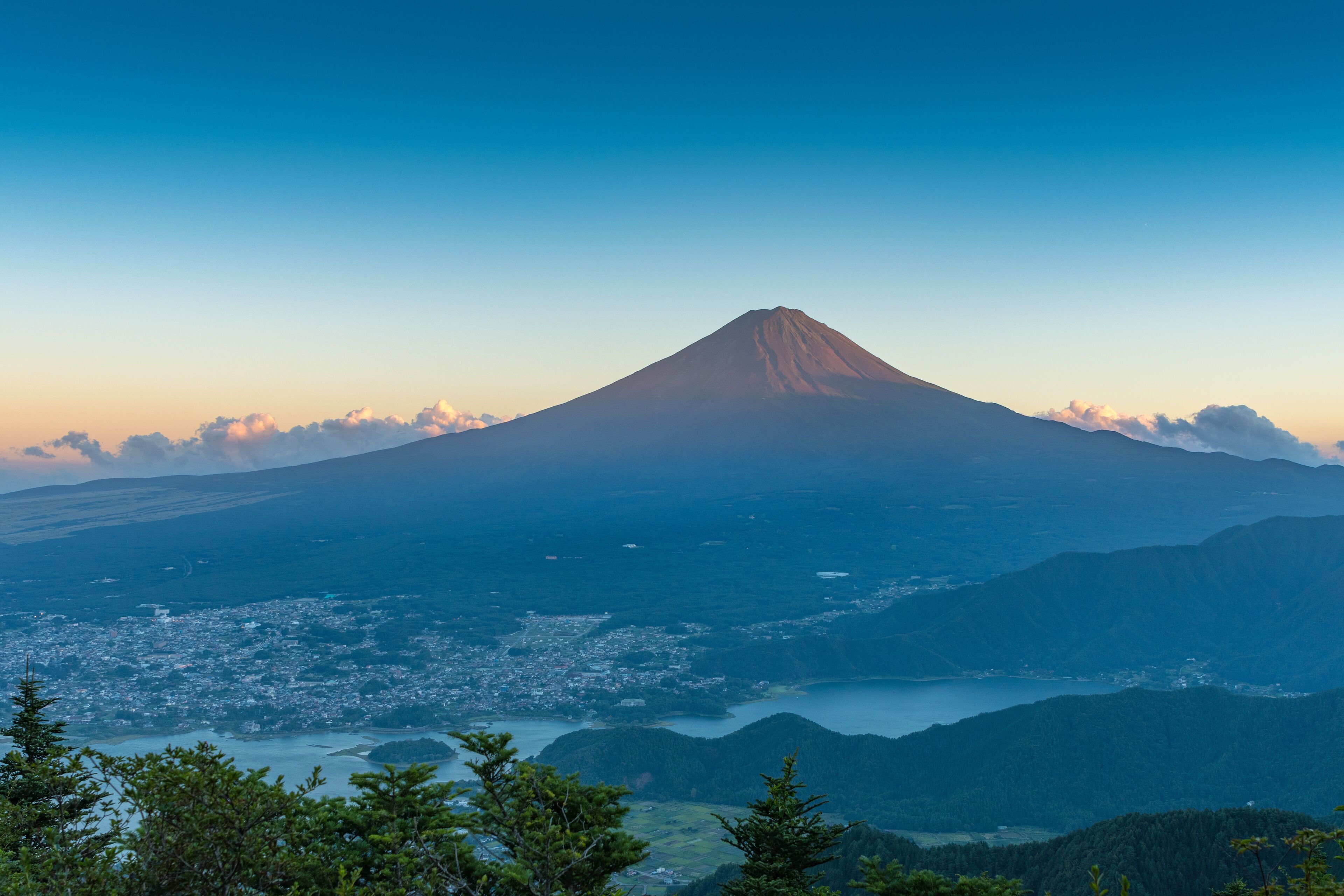A mountain with a conical shape, a valley with a town, and a body of water.