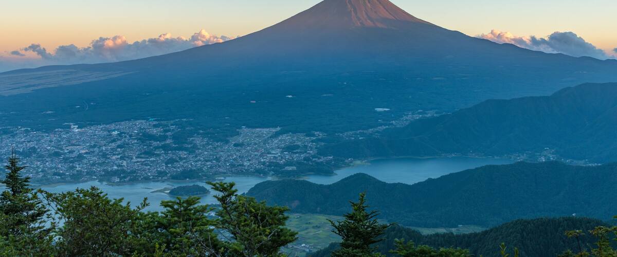 A mountain with a conical shape, a valley with a town, and a body of water.