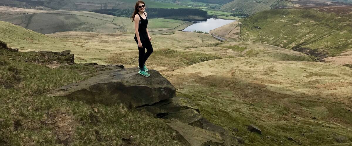 A person standing on a rock with a view of rolling hills and a lake in the distance.