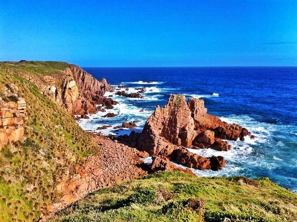 A coastal landscape with rocky cliffs and waves crashing against them.