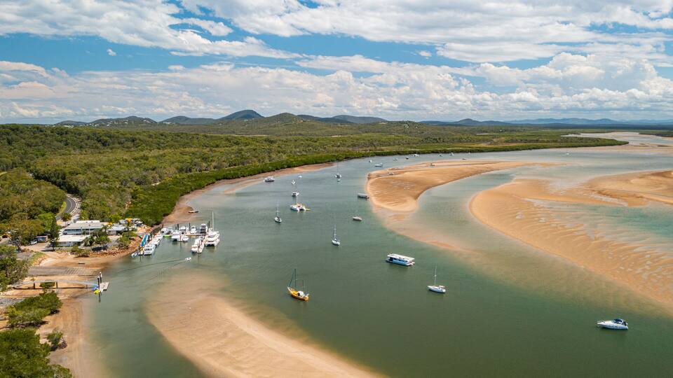 A coastal area with boats, a sandy beach, and a forested landscape.