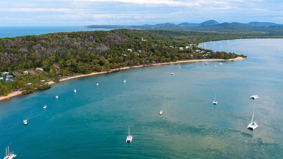 A coastal landscape with a beach, boats, and a forested area.
