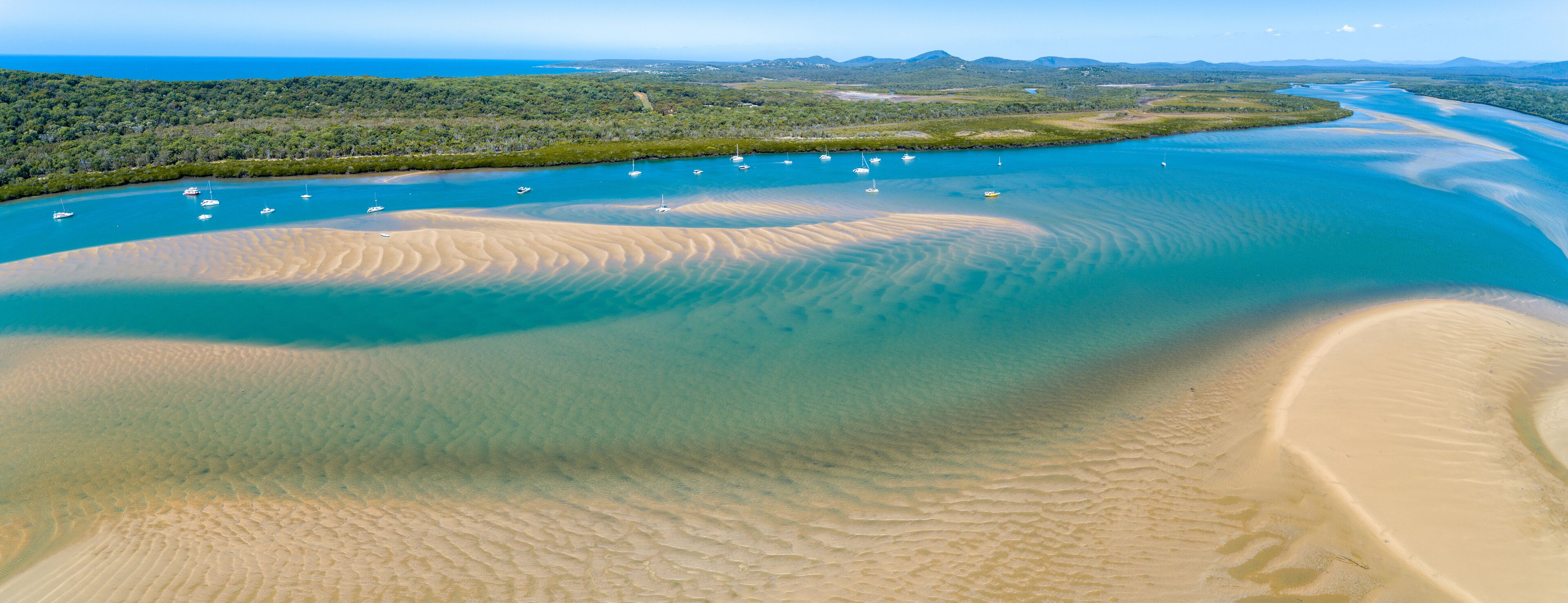 Paisagem costeira com uma praia de areia, um rio e várias embarcações.
