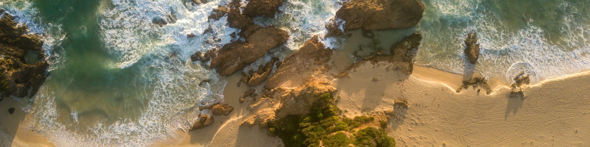 An aerial view of a coastal landscape with rocky outcrops, sandy beach, and dense greenery.