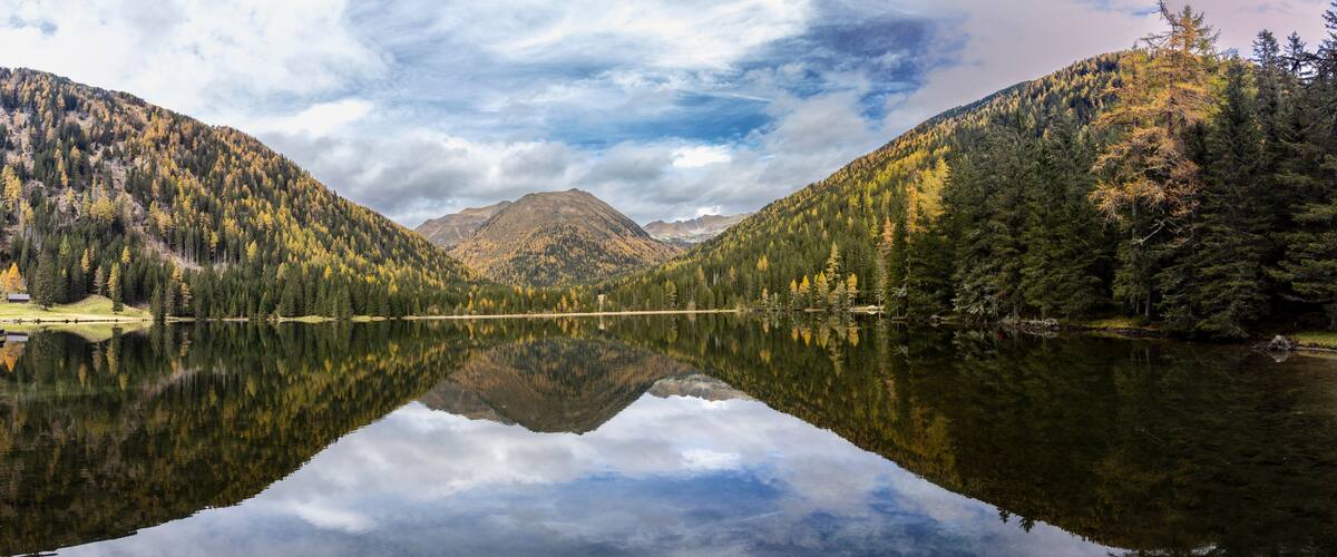 A mountain lake with reflections of trees and a cabin.
