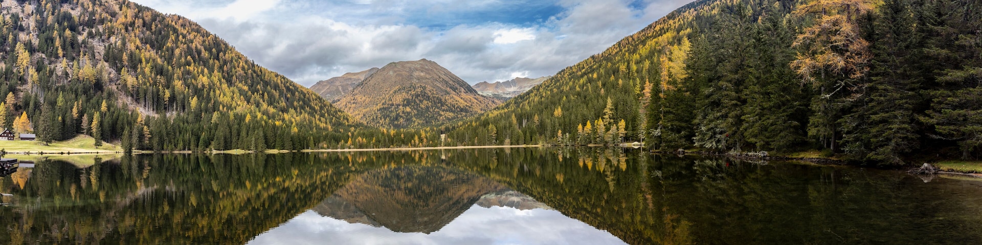 A mountain lake with reflections of trees and a cabin.