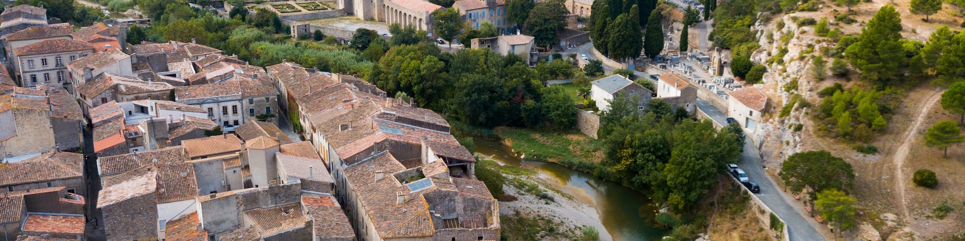A historic town with terracotta-roofed buildings, a river, and a stone bridge.