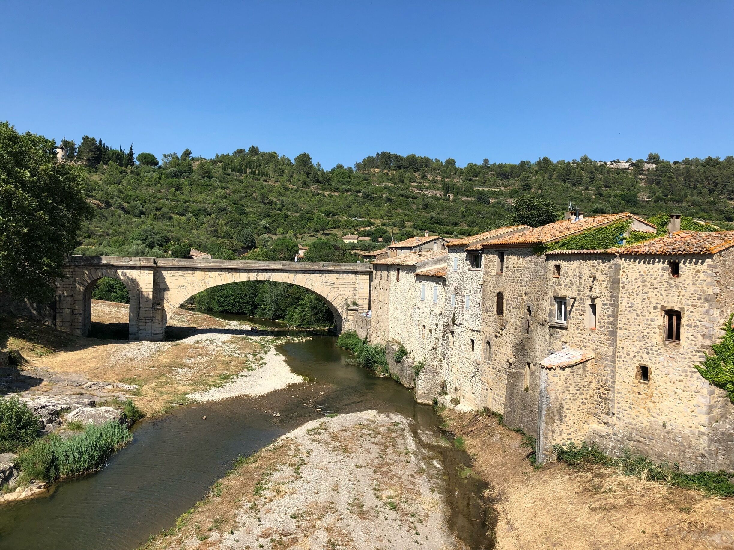 A stone bridge over a river, surrounded by stone buildings and lush greenery.
