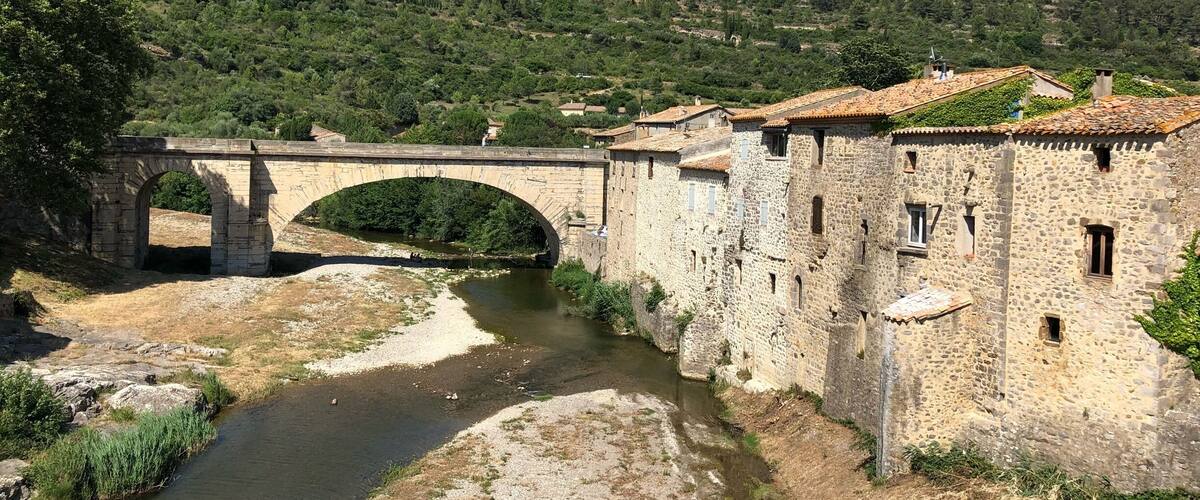 A stone bridge over a river, surrounded by stone buildings and lush greenery.