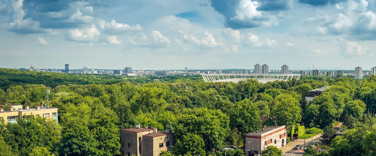 A cityscape with a bridge, dense greenery, and modern buildings.