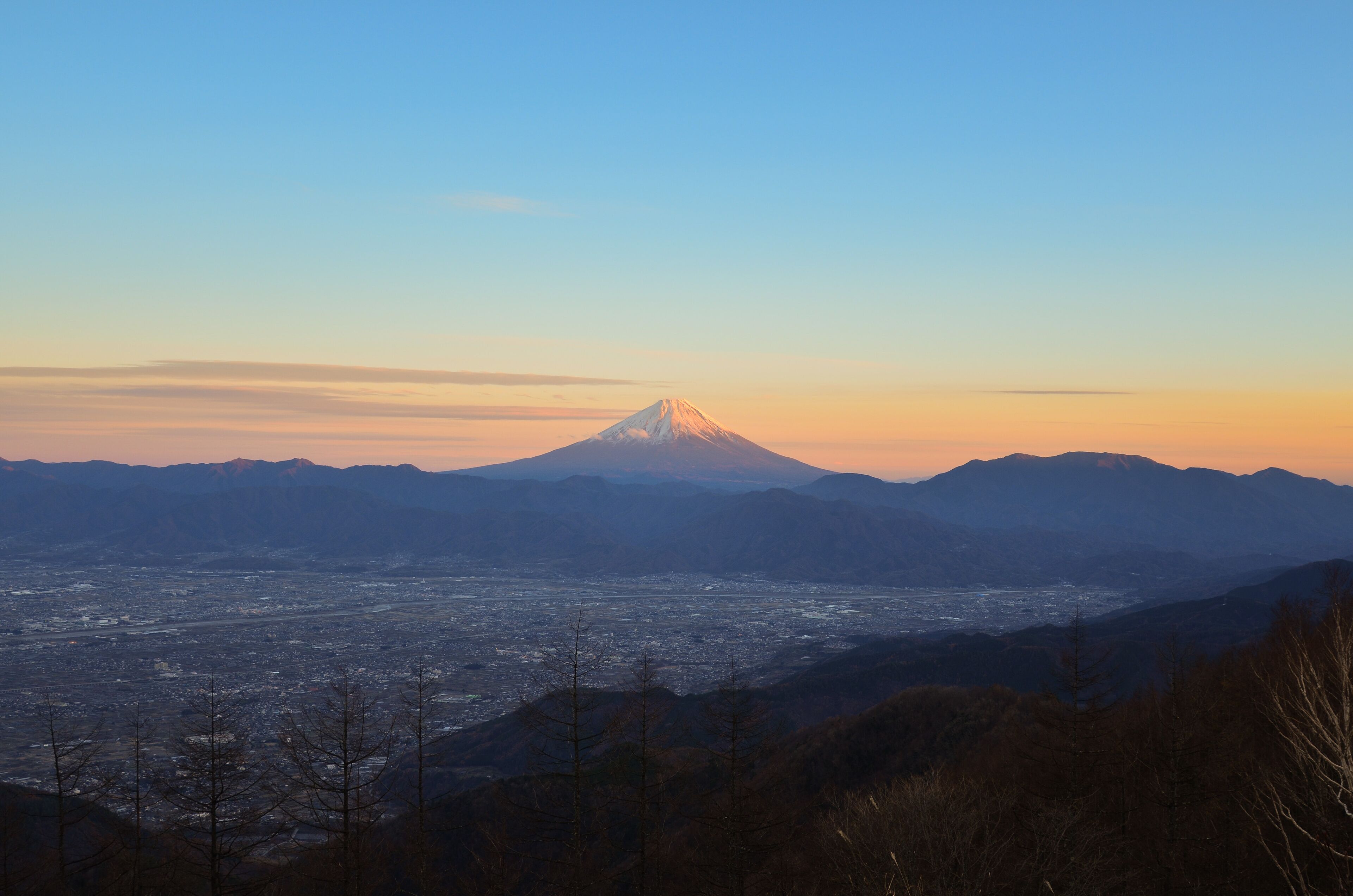 A mountain with a snow-capped peak, a valley with a city, and distant mountains.