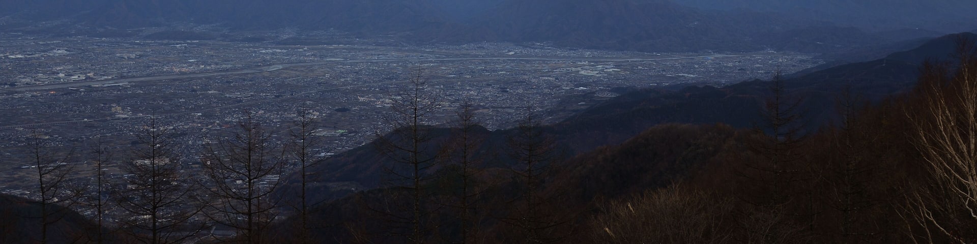 A mountain with a snow-capped peak, a valley with a city, and distant mountains.
