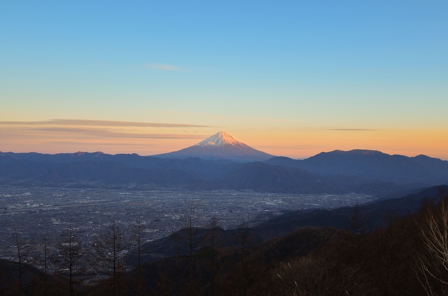 A mountain with a snow-capped peak, a valley with a city, and distant mountains.