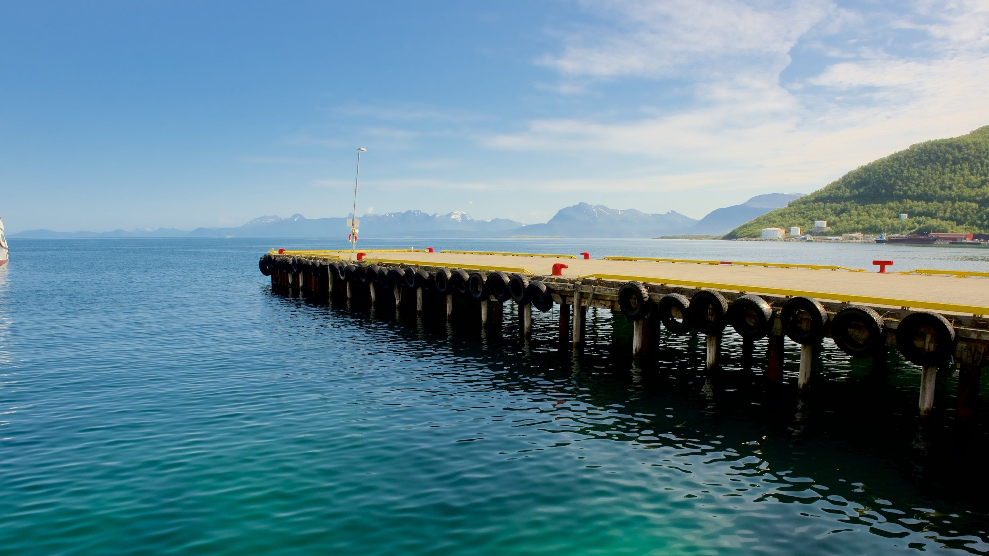 A pier extending into calm waters with a mountainous backdrop.