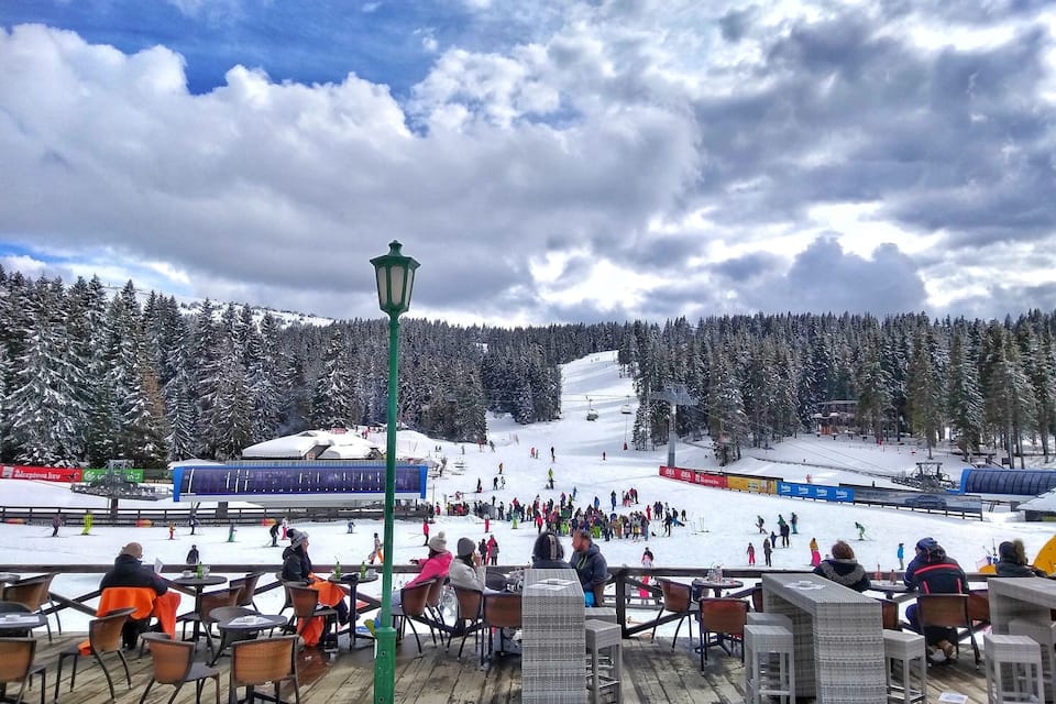 A snowy ski slope with people skiing and snowboarding, surrounded by snow-covered trees.