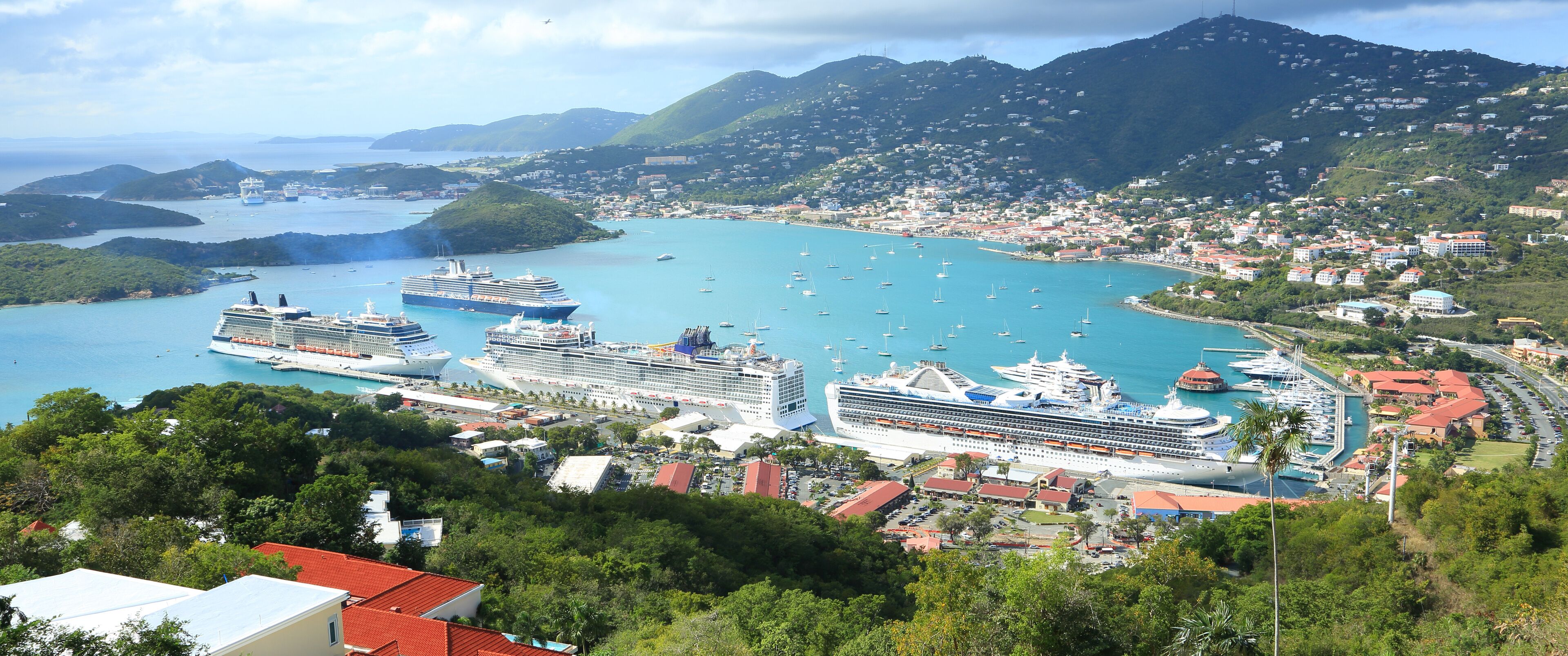 A coastal town with cruise ships docked in a bay, surrounded by lush green hills and clear blue waters.