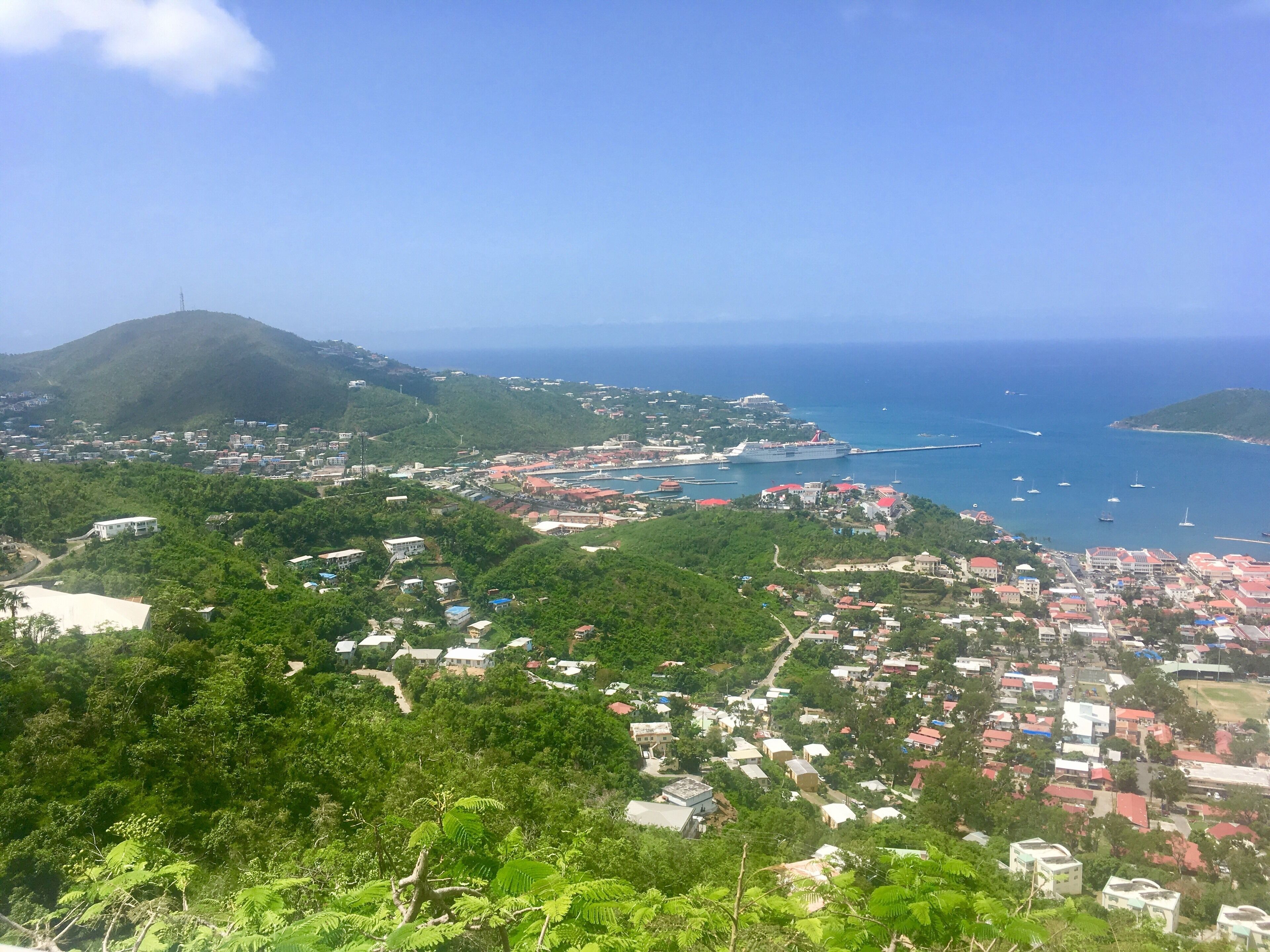 A coastal town with a harbor, surrounded by hills and lush greenery.