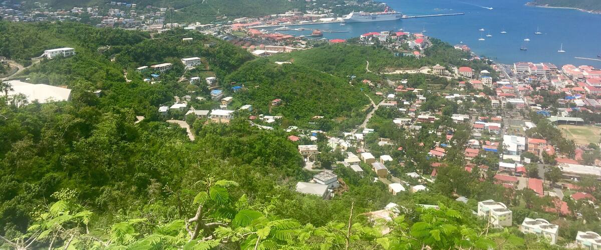 A coastal town with a harbor, surrounded by hills and lush greenery.