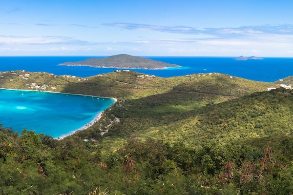 Eine Küstenlandschaft mit türkisfarbenem Wasser, grünen Hügeln und einer kleinen Insel in der Ferne.