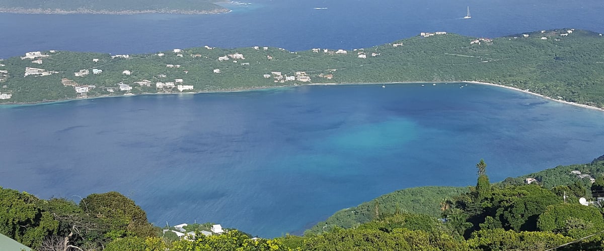 A coastal landscape with a clear blue sea, green hills, and scattered buildings.