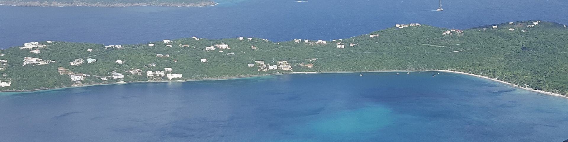 A coastal landscape with a clear blue sea, green hills, and scattered buildings.