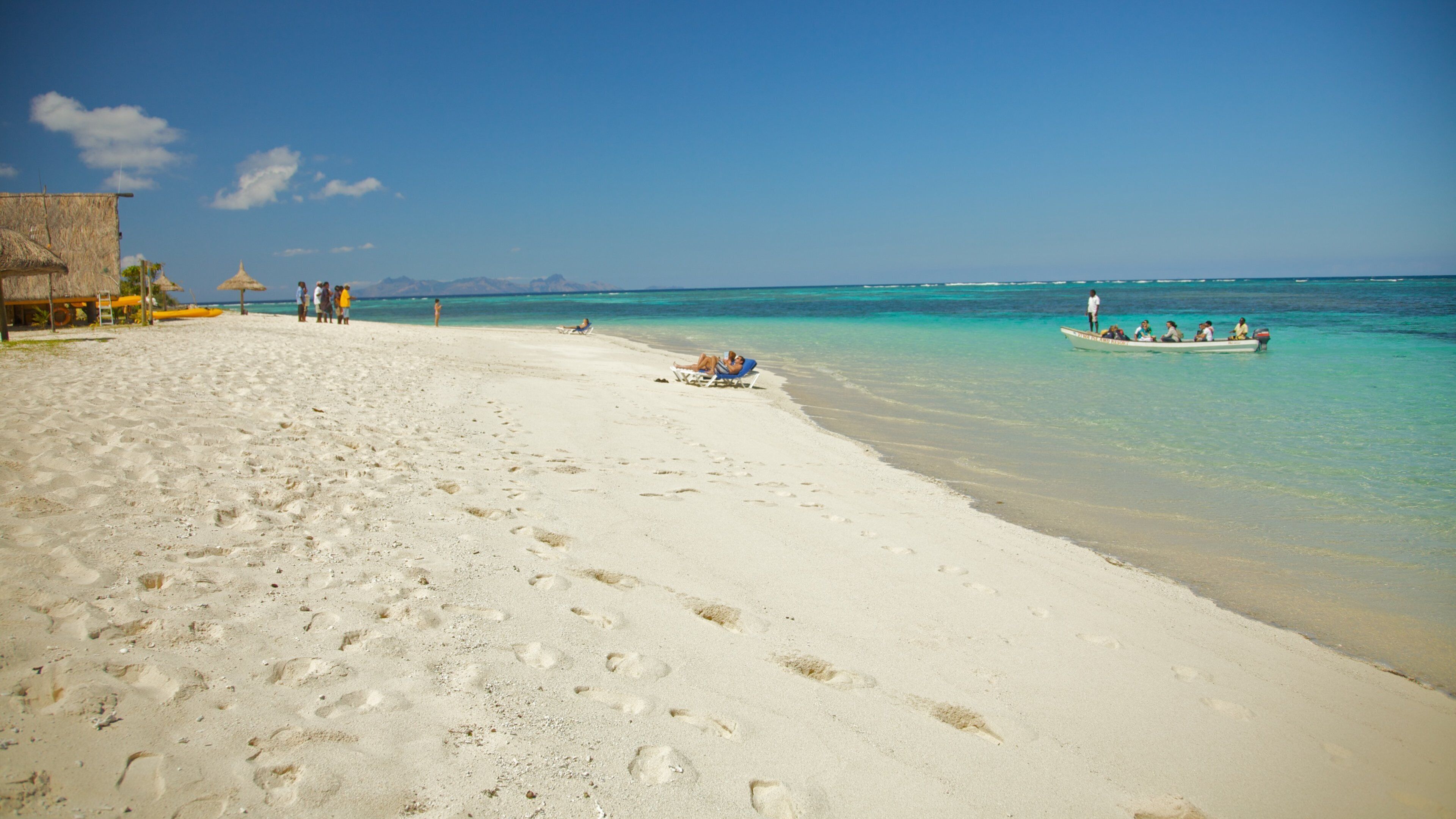 A beach with footprints, a boat, and a thatched-roof structure.