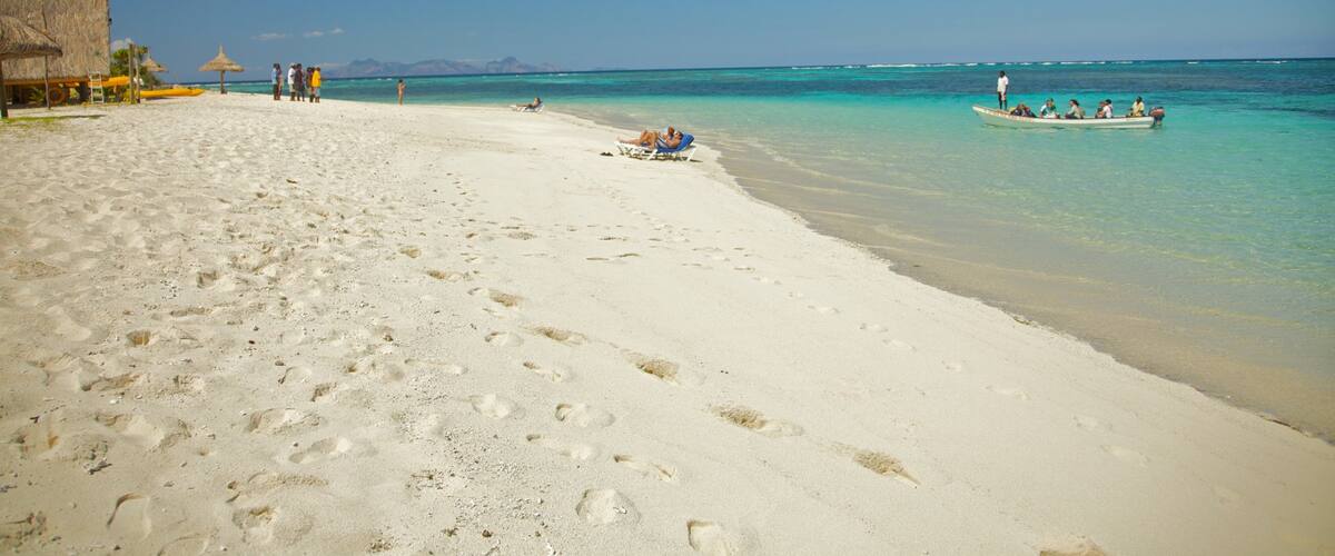 A beach with footprints, a boat, and a thatched-roof structure.