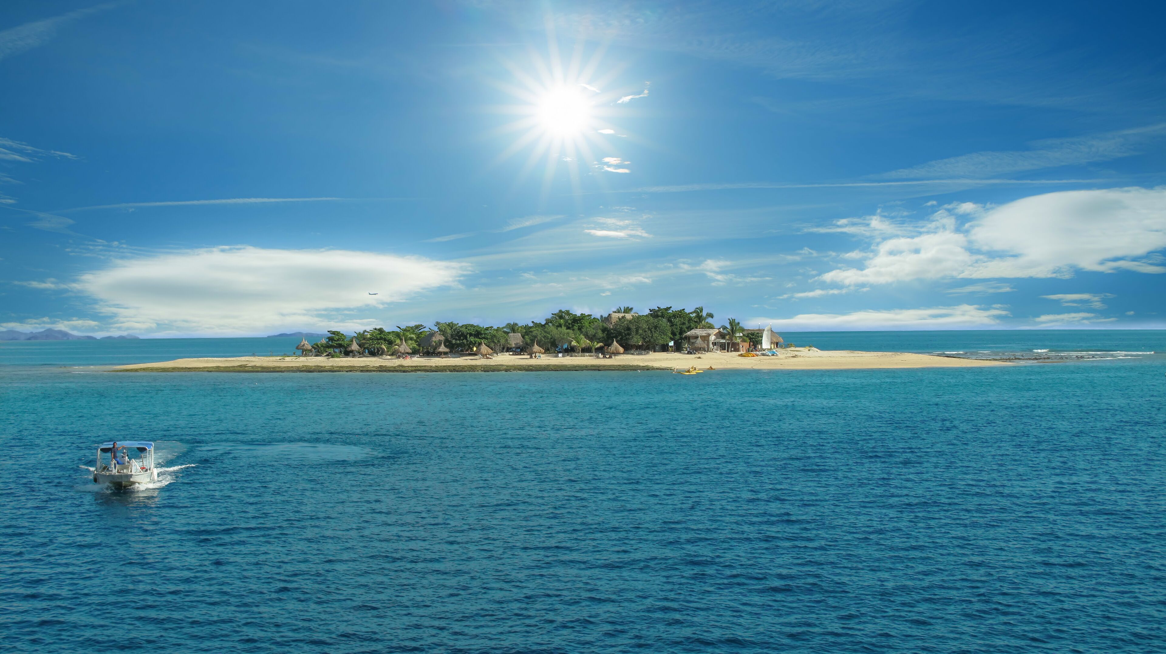 A tropical island with clear blue waters, a boat, and a sunny sky.
