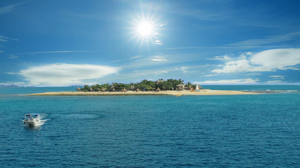 A tropical island with clear blue waters, a boat, and a sunny sky.