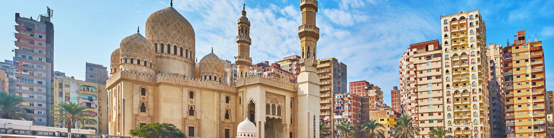 A historic mosque with domes and minarets, surrounded by modern high-rise buildings.