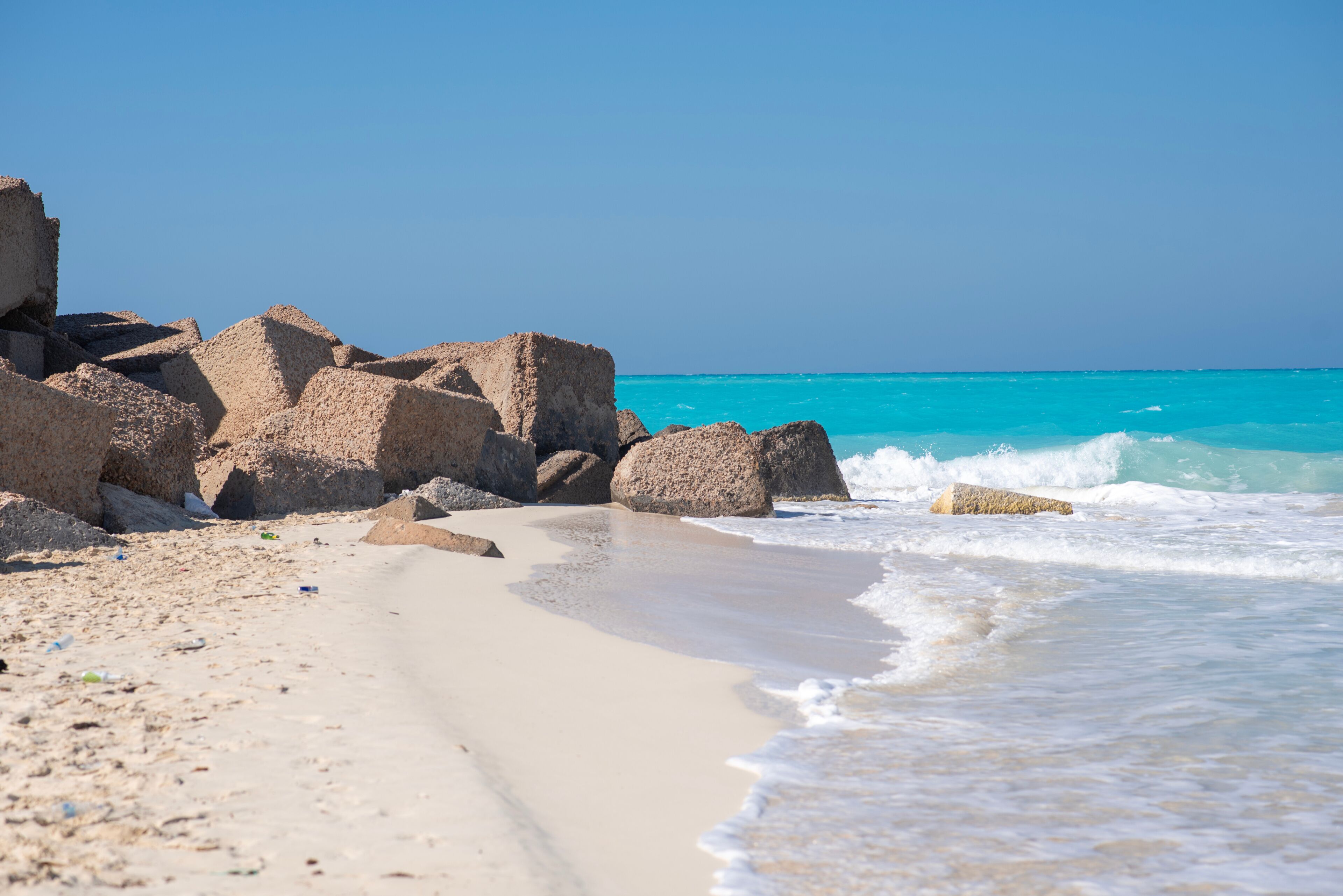 A sandy beach with large rocks and turquoise ocean waves.