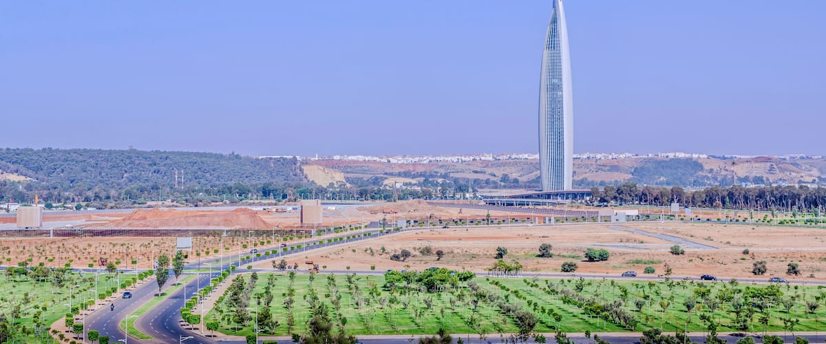 A modern skyscraper, a highway, and a hilly landscape with sparse vegetation.