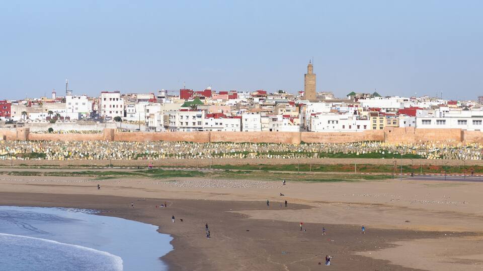 A coastal cityscape with a prominent tower, a sandy beach, and a densely packed urban area with colorful buildings.