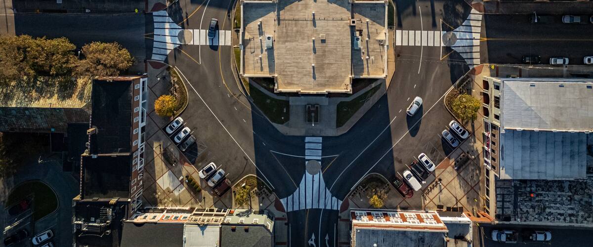 An aerial view of a roundabout with a central plaza, surrounded by buildings and parked cars.