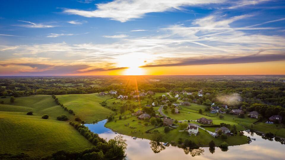 A sunset over a rural landscape with a river, houses, and fields.