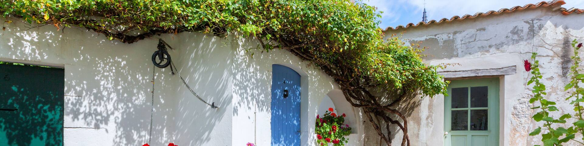 A white building with a blue door, a green door, and a bicycle parked in front.