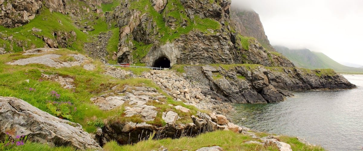 A rugged coastal landscape with a rocky cliff, a tunnel entrance, and a calm sea.