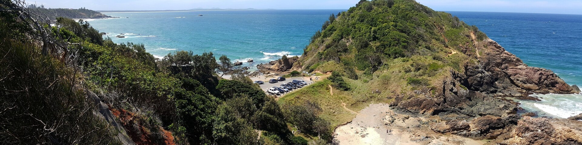 Paisagem costeira com uma colina rochosa imponente, uma praia e o oceano.