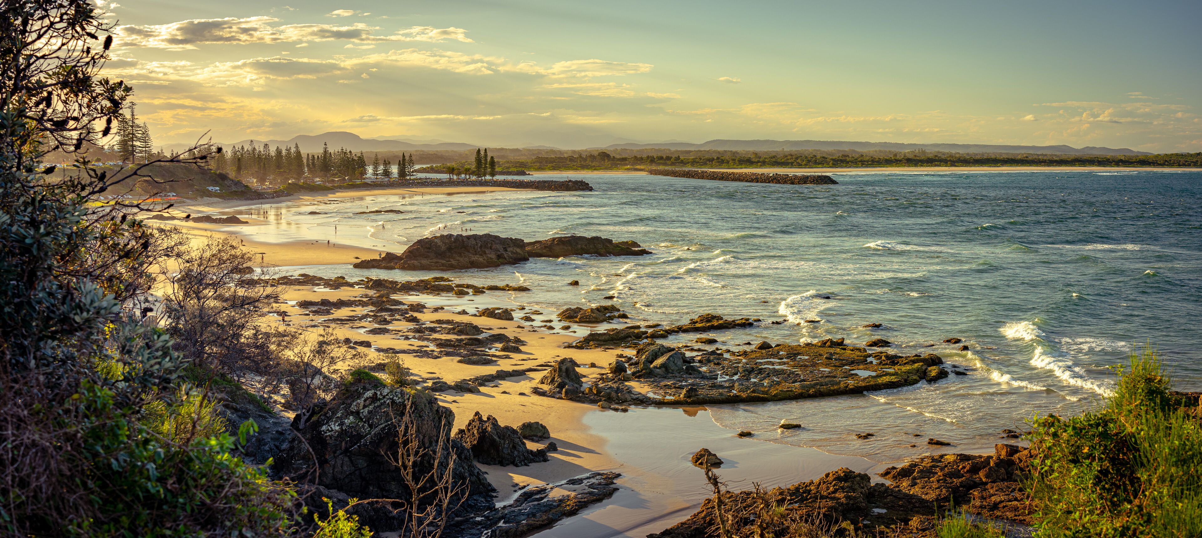 A rocky shoreline with waves, a distant tree line, and a clear sky.