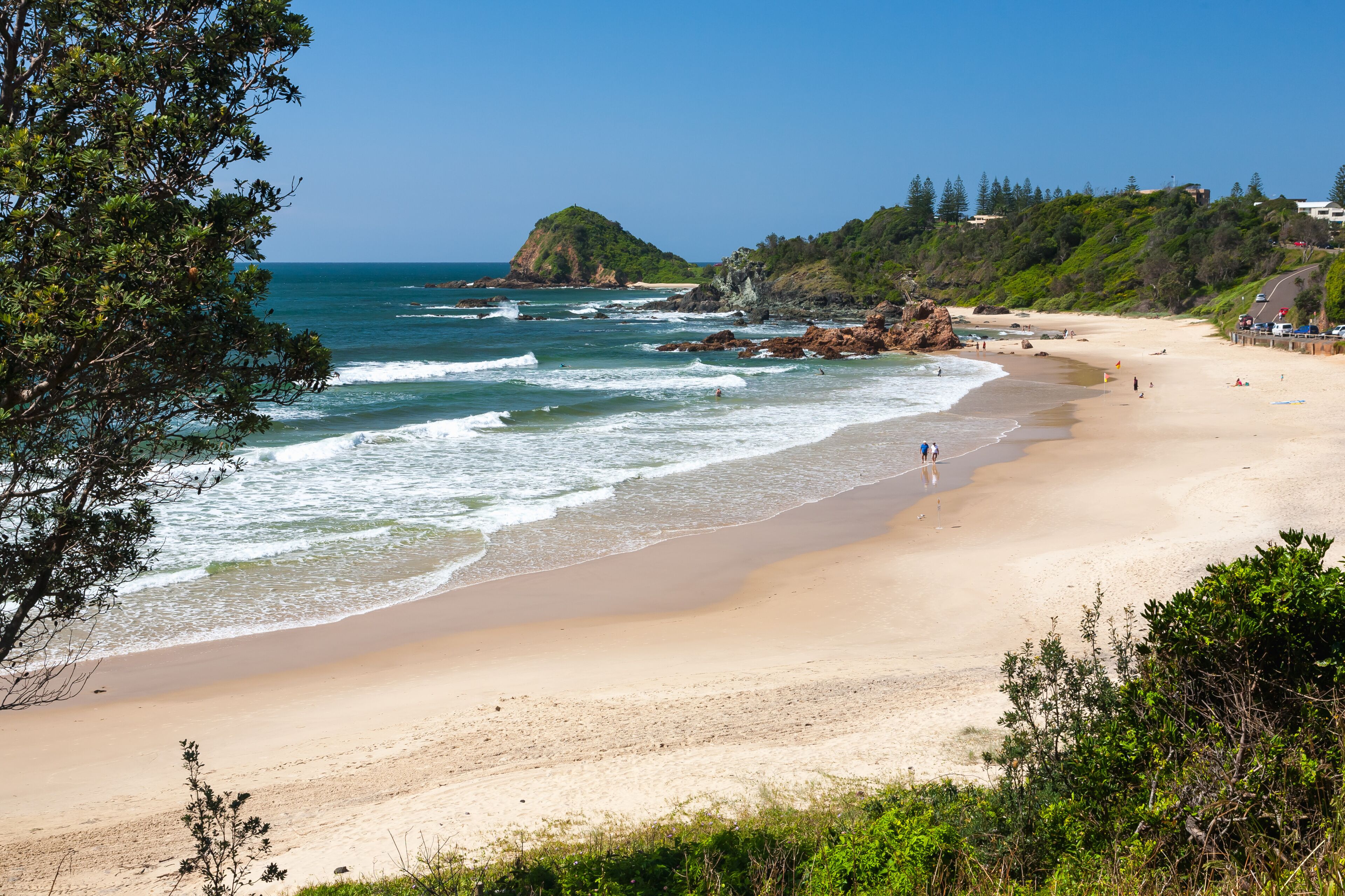 Uma praia com ondas, um afloramento rochoso e uma colina arborizada.